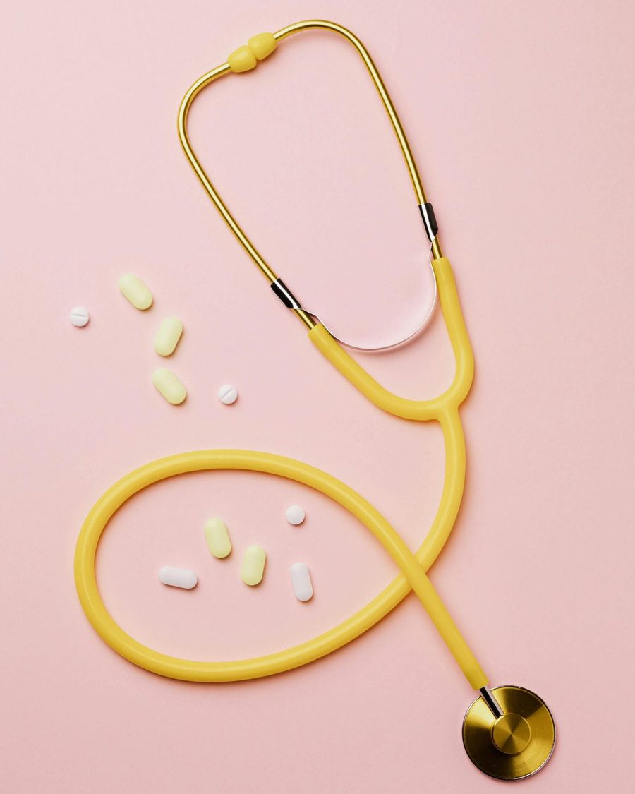 Gelbes Stethoskop mit Tabletten und Kapseln auf rosa Hintergrund
