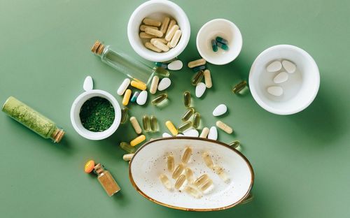 Kapseln, Tabletten und Pflanzenpulver in Schalen auf grünem Untergrund